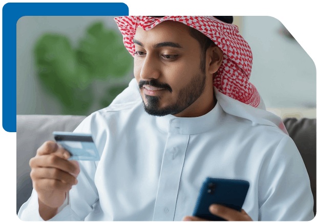 Saudi man holding a credit card and smartphone, appearing to make an online purchase or verify a mobile banking transaction.