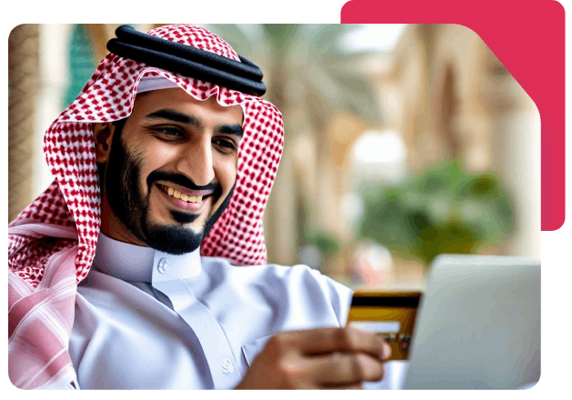 Smiling Saudi man in traditional attire holding a credit card and using a laptop, representing secure online payments with Network.