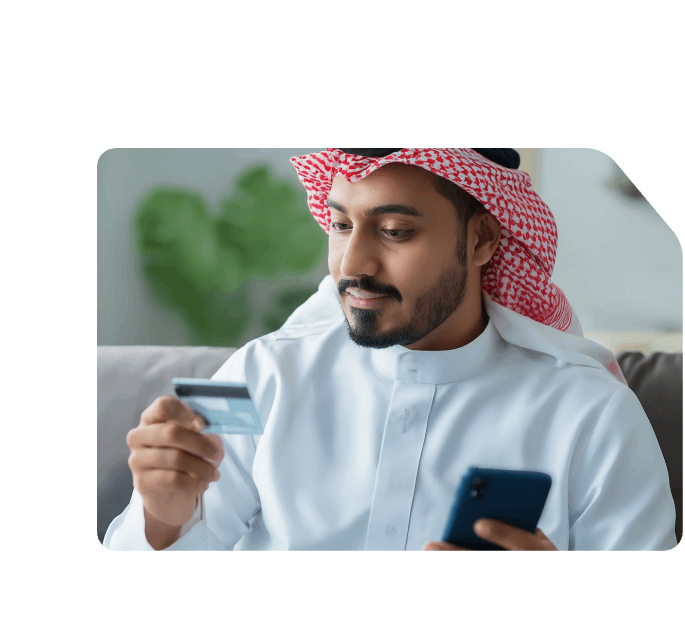 Saudi man holding a Network payment card and smartphone, appearing to make a secure online purchase or mobile transaction.