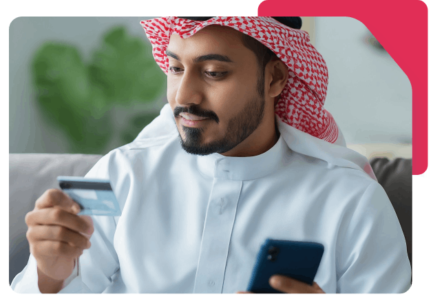 Saudi man holding a Network payment card and smartphone, appearing to make a secure online purchase or mobile transaction.