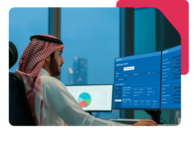 Saudi man in traditional attire working at dual monitors displaying Network dashboards and analytics in a modern office.