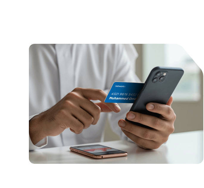 Saudi man holding a Network payment card and smartphone, appearing to make an online transaction or digital payment.