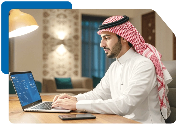 Saudi man in thobe uses credit card and laptop for online financial activity.