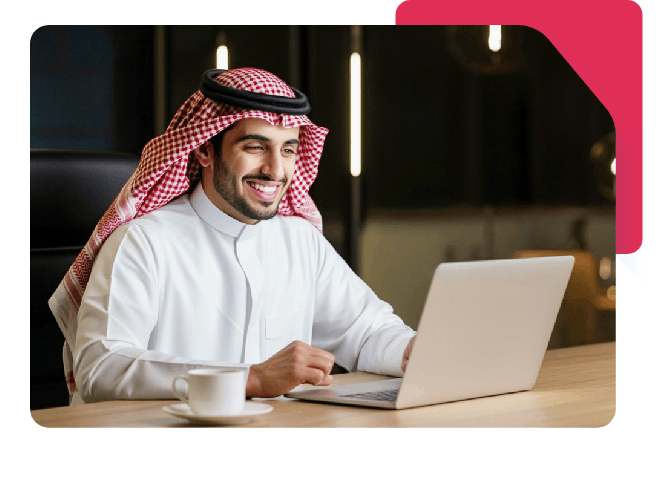 Smiling Saudi man working on laptop in a modern office setting.